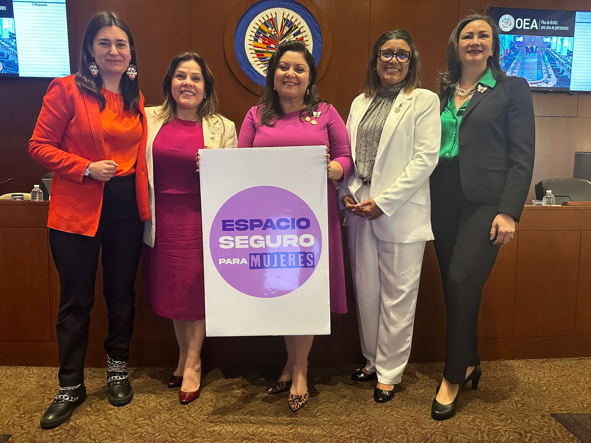 cinco mujeres representantes ante la OEA con un rótulo con la frase Espacio Seguro para Mujeres